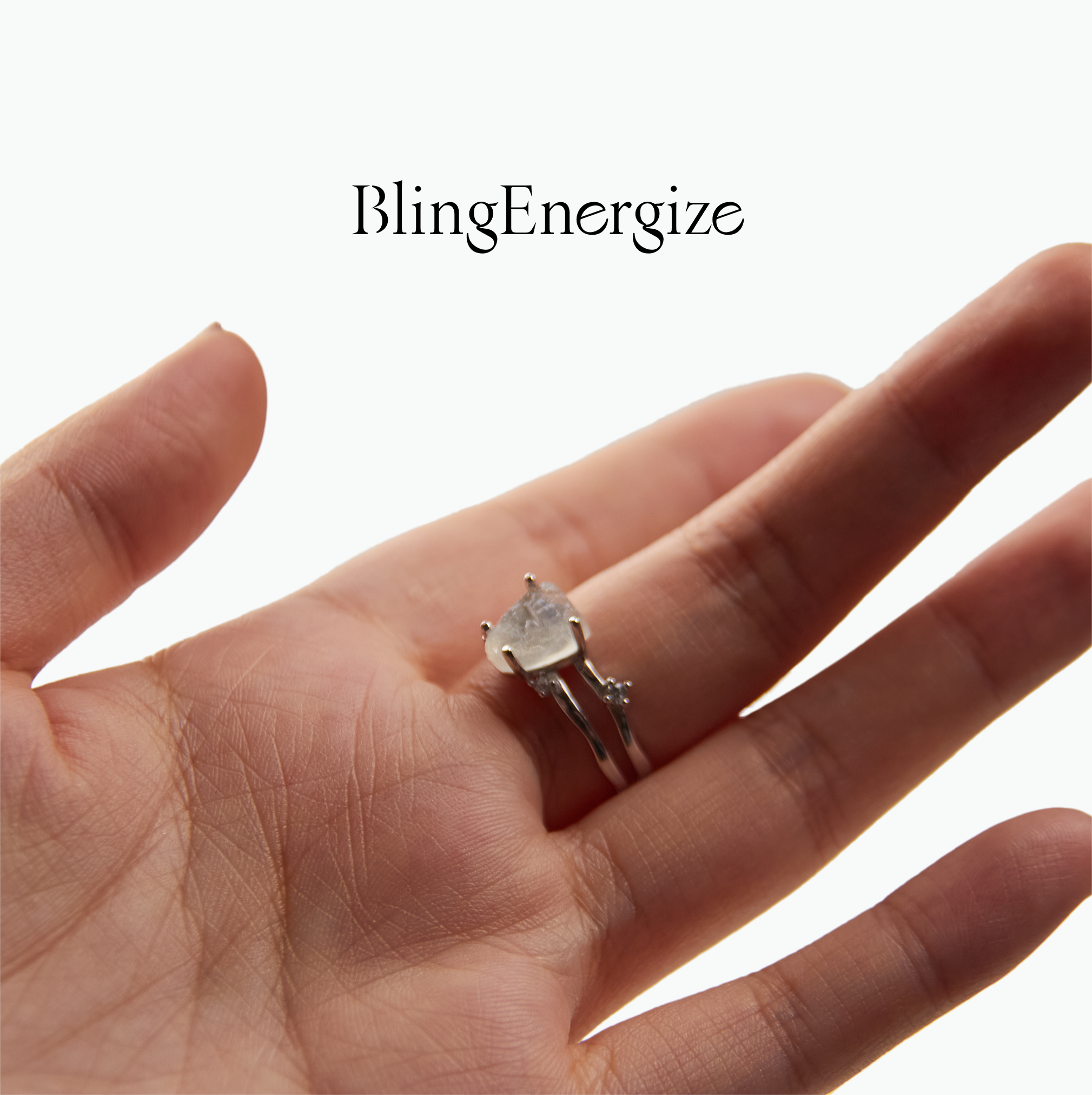 Hand wearing a silver ring with a clear gemstone on a white background, featuring the brand 'BlingEnergize'.