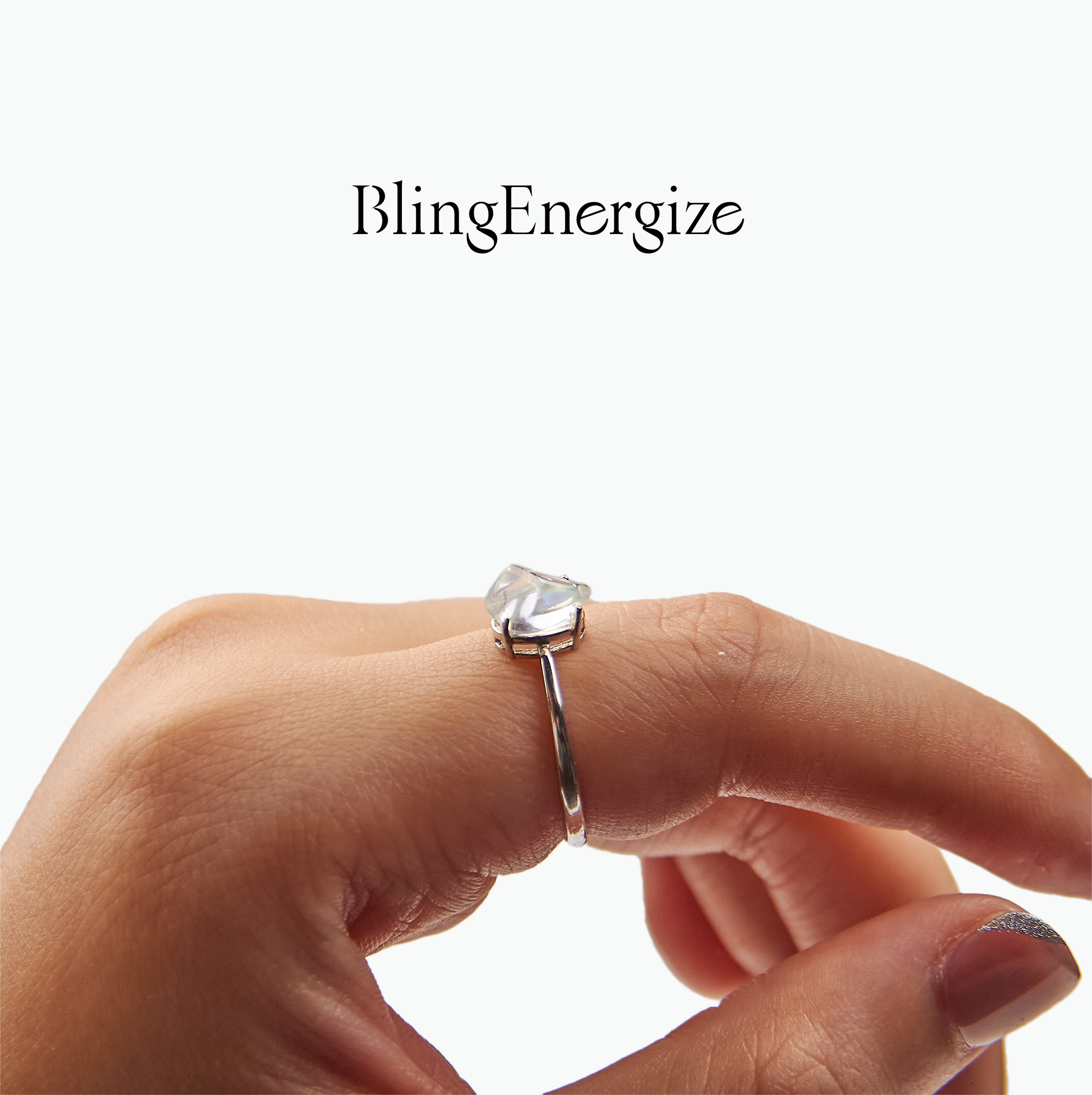 Silver ring with a heart-shaped gemstone on a finger, branded 'BlingEnergize'.