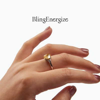 Hand wearing a ring with a Golden Rutilated Quartz on a white background, featuring the brand 'BlingEnergize'.
