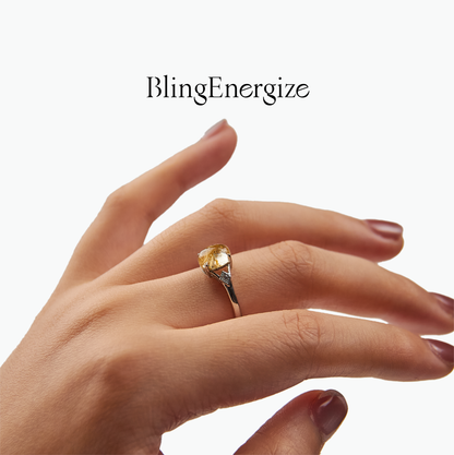 Hand wearing a ring with a Golden Rutilated Quartz on a white background, featuring the brand 'BlingEnergize'.