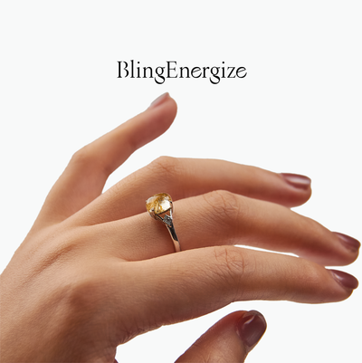 Hand wearing a gold ring with a gemstone on a white background, featuring the brand 'BlingEnergize'.