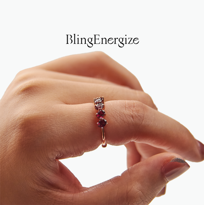 Hand wearing a ring with garnet gemstones on a white background, featuring the brand 'BlingEnergize'.
