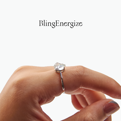 Silver ring with a heart-shaped gemstone on a finger, branded 'BlingEnergize'.
