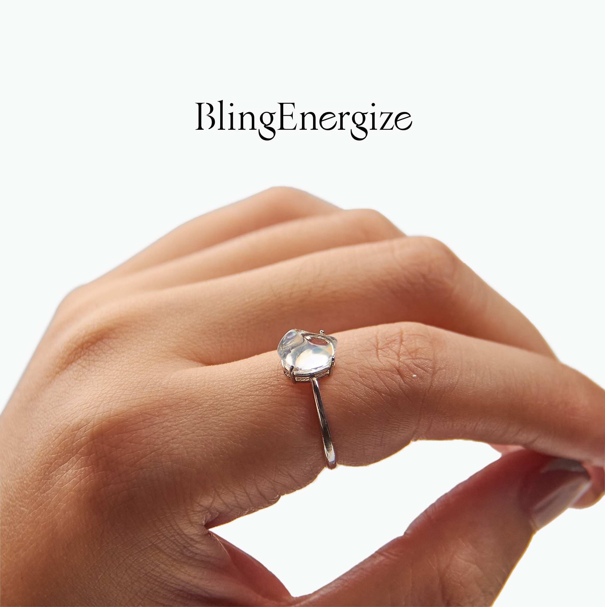 Hand wearing a silver ring with a clear gemstone on a white background, featuring the brand 'BlingEnergize'.