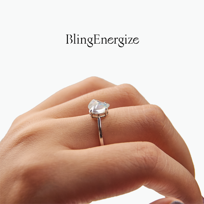Hand wearing a ring with a moonstone gemstone on a white background, featuring the brand 'BlingEnergize'.
